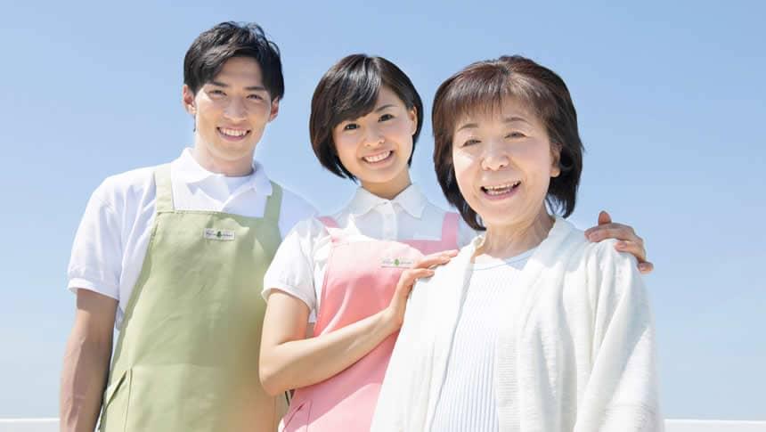 年配の女性の肩に手をおいて微笑む介護職員の男女