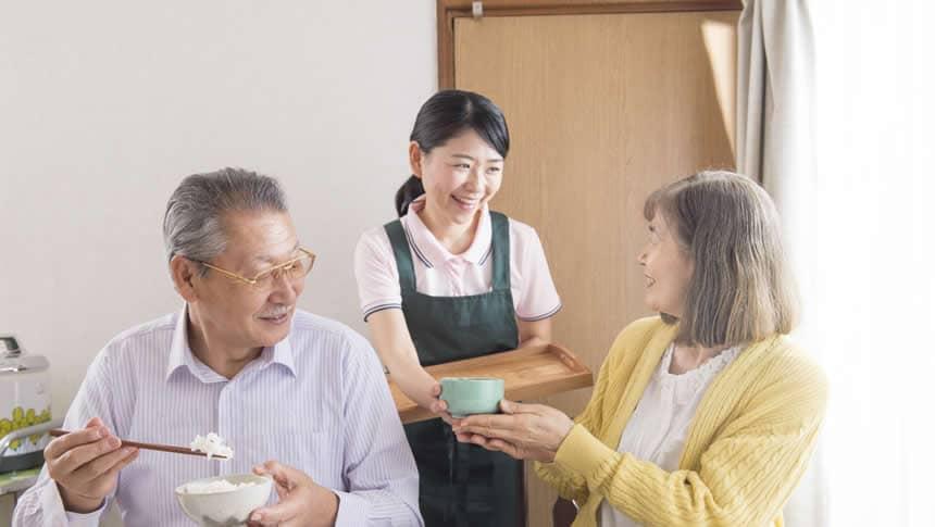 年配夫婦の食事のお世話をする介護職員
