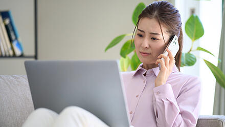 ノートパソコンに向かいながら電話をする女性
